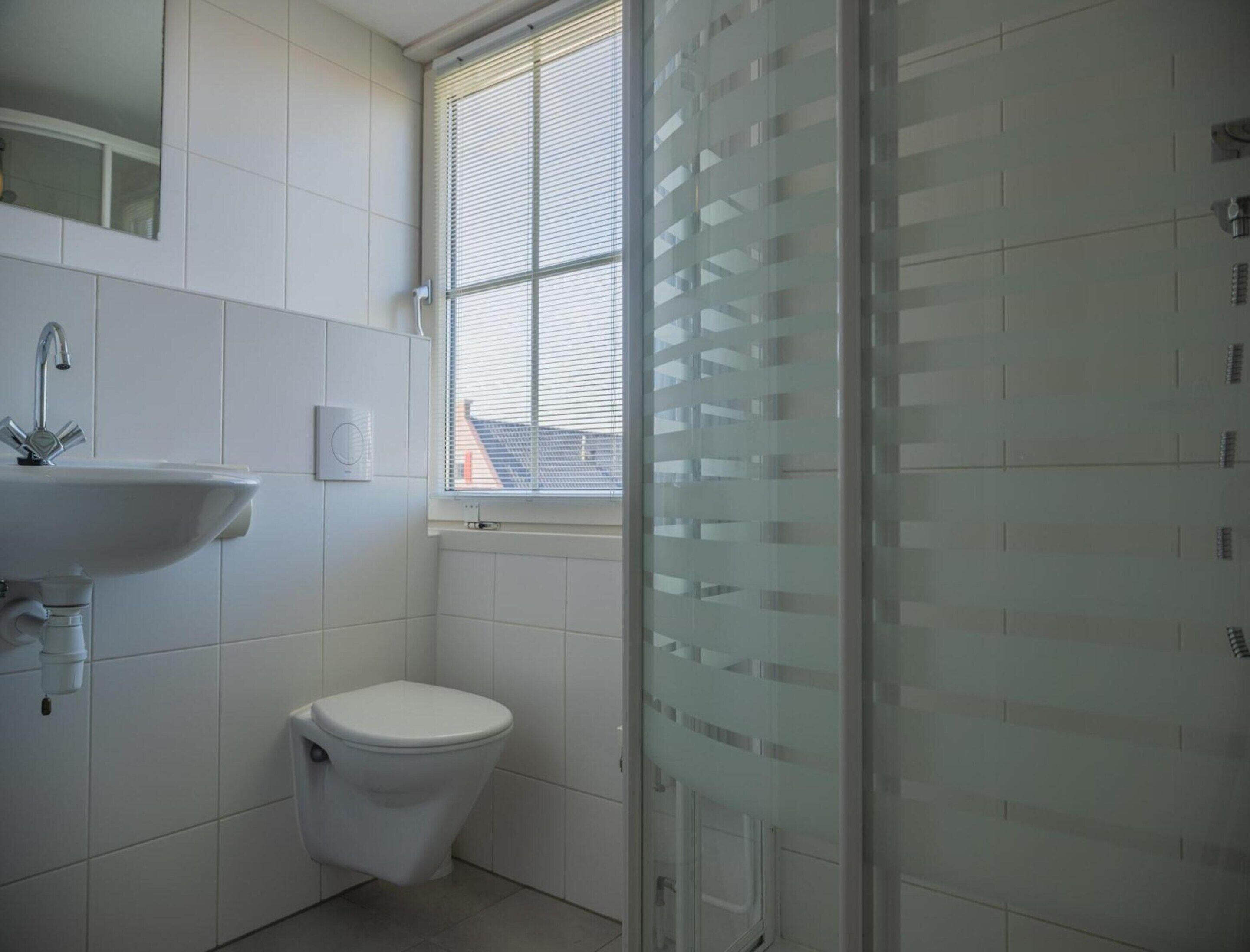 Un baño con lavamanos blanco, inodoro y ventana con persianas.