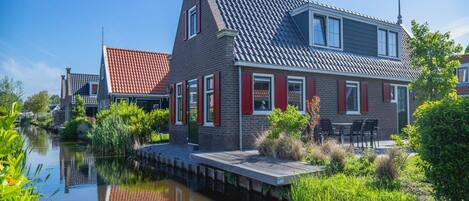 A canal-side house with a red-tiled roof, a brick facade, and a small dock extending into the water.