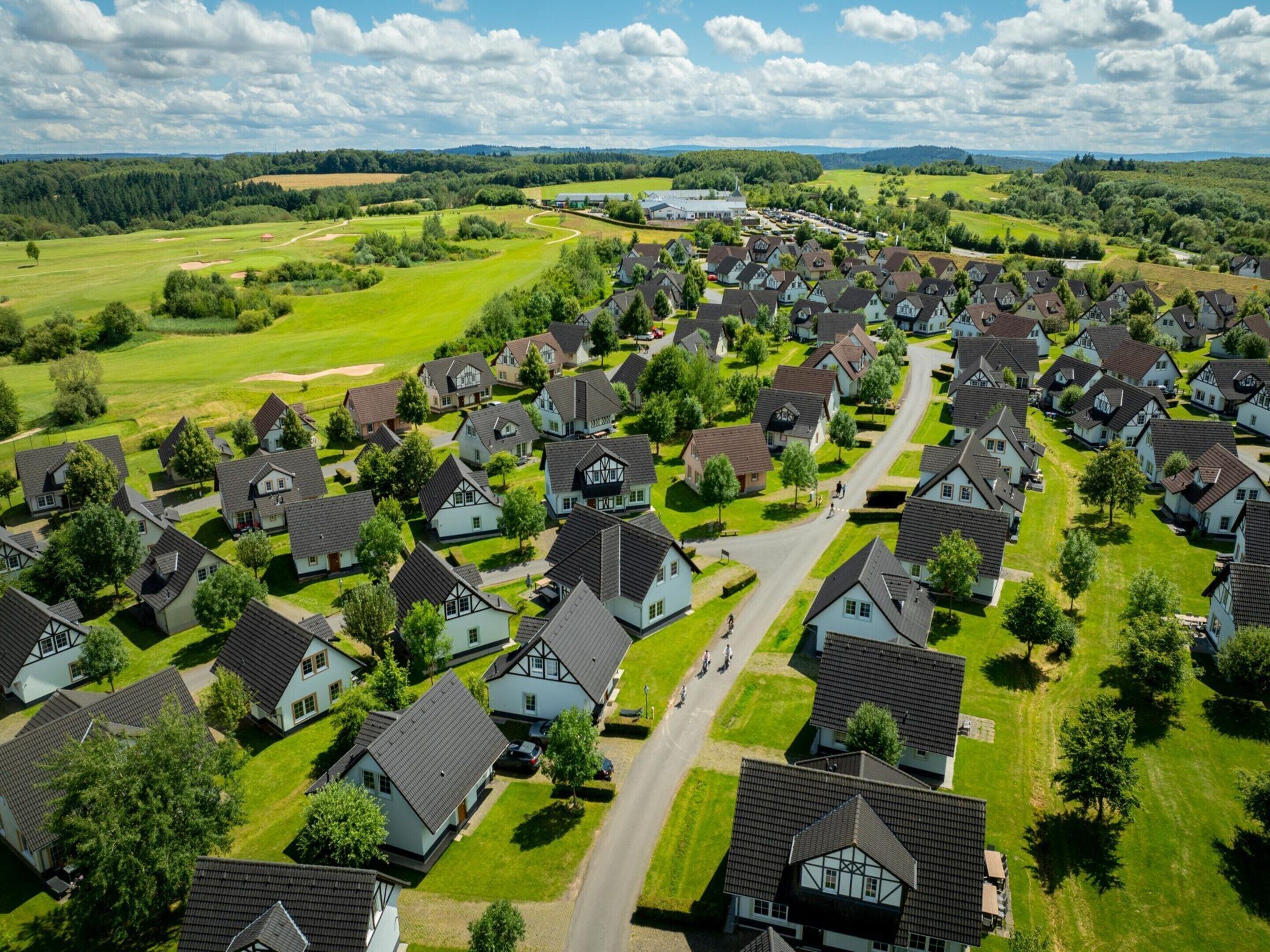A residential area with houses arranged in a grid pattern, surrounded by green fields and a golf course.