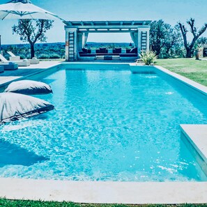 Ein rechteckiger Pool mit einer Pergola und Sitzgelegenheit.