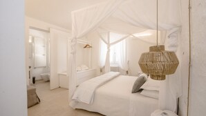 Un dormitorio con cama a dosel, una lámpara colgante de ratán y un baño blanco al fondo.