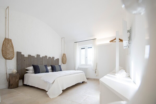 A bedroom with a bed, bedside tables, a hanging light, a window, and a radiator.