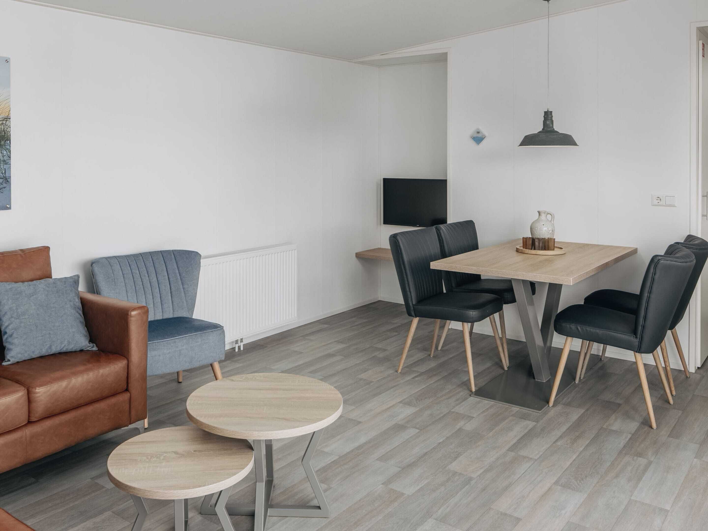Een moderne woonkamer met een bruine leren bank, een blauwe fauteuil en twee ronde houten tafels.