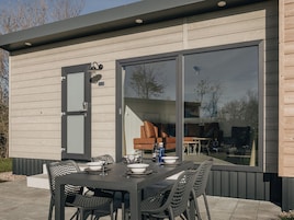 An outdoor dining area with a table set for four, surrounded by chairs, and a large window reflecting the interior.