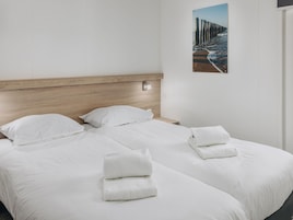 A hotel room with two beds, white linens, a wooden headboard, a nightstand, and a framed picture on the wall.