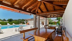 A covered outdoor area with wooden benches and tables, a pool, and a view of the surrounding landscape. - Mobile Home in Banjole Near Centinera Beach (Medulin)