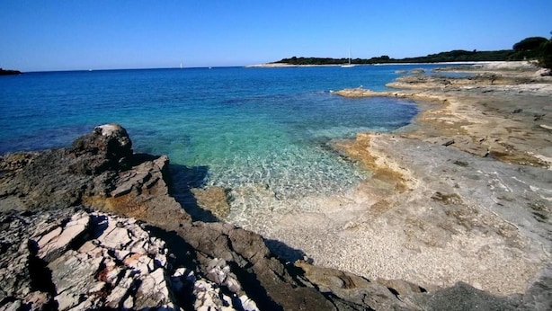 A rocky shoreline with clear blue water and a distant view of a sailboat. - Mobile Home in Banjole Near Centinera Beach (Medulin)