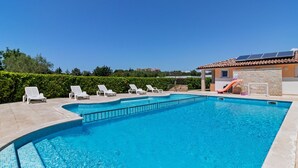 A swimming pool with white lounge chairs and a small slide, surrounded by a stone wall and a building with a tiled roof. - Mobile Home in Banjole Near Centinera Beach (Medulin)