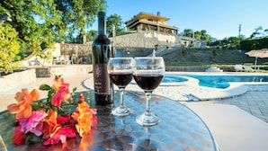 Une table avec une bouteille de vin et deux verres, un arrangement floral et une vue sur un bâtiment depuis le bord de la piscine.