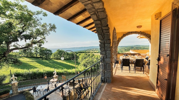 Une terrasse extérieure agrémentée d’arches en pierre, une table dressée pour le repas et une vue sur un paysage verdoyant.