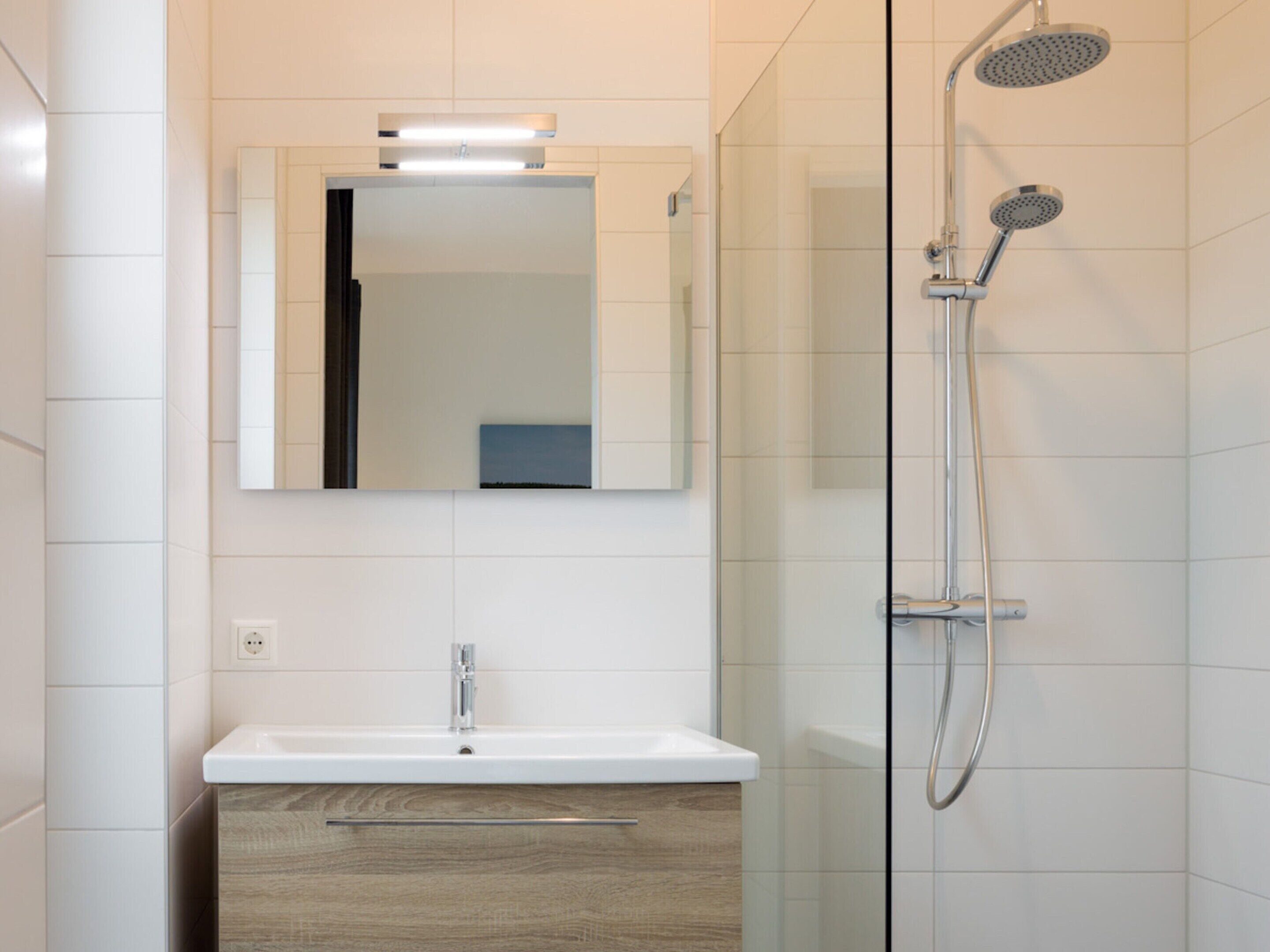 A modern bathroom with a glass shower enclosure, a white sink with a wooden cabinet, and a mirror above the sink.