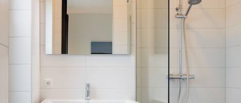 A modern bathroom with a glass shower enclosure, a white sink with a wooden cabinet, and a mirror above the sink.