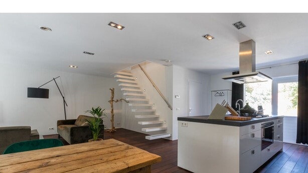 A modern kitchen with a central island, a staircase, and a dining area with a wooden table and chairs. - Beautiful Well Equipped Apartment Near the Beach (Domburg)