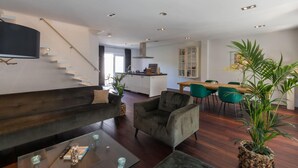 A modern living room with a sofa, armchair, and coffee table, a dining area with chairs, a kitchen in the background, and a staircase. - Beautiful Well Equipped Apartment Near the Beach (Domburg)