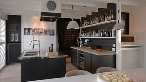 Una cucina moderna con isola centrale, angolo bar con scaffali pieni di bottiglie e zona pranzo con tavolo e sedie bianche.
