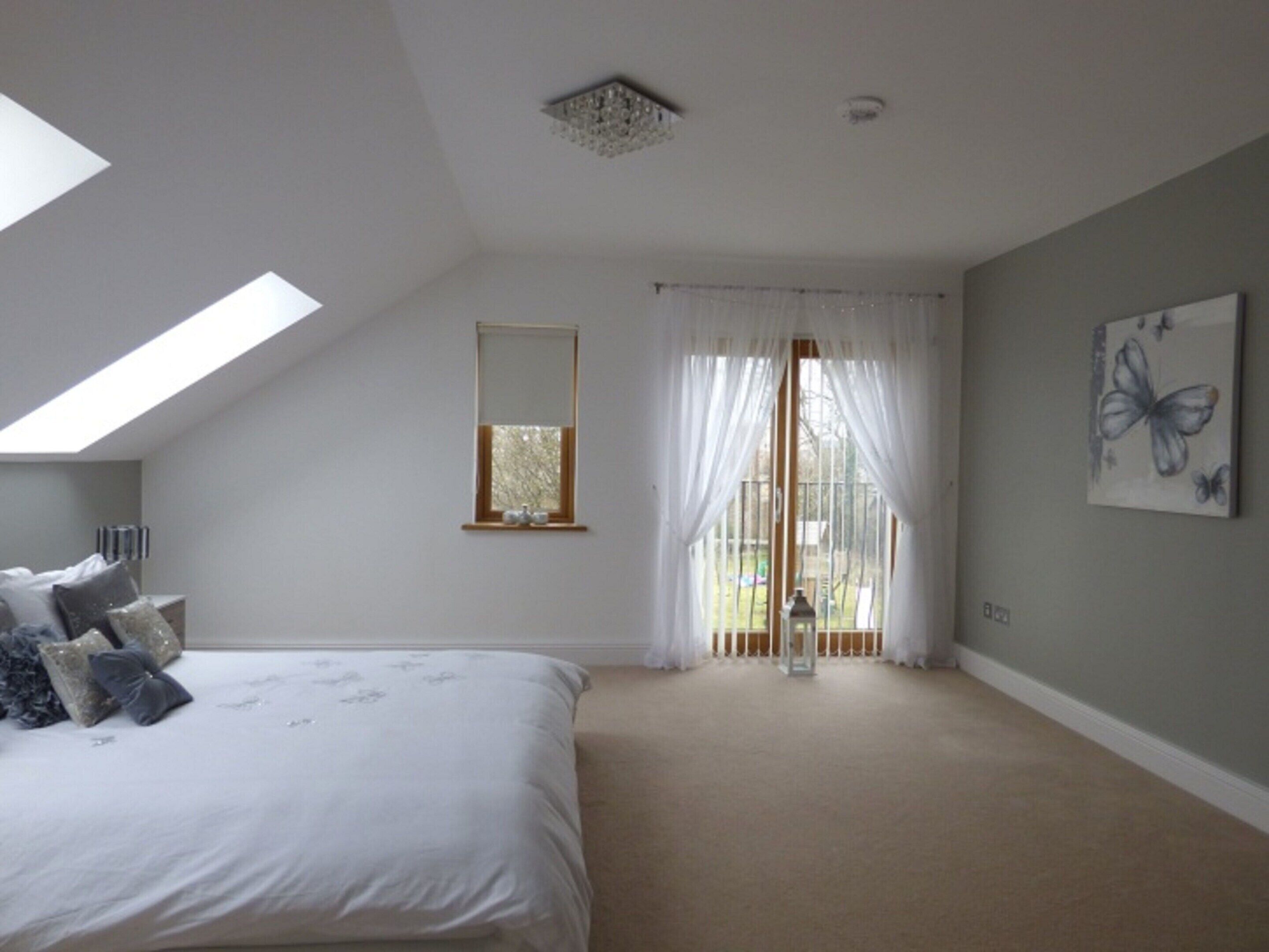 Ein Schlafzimmer mit Bett, Dachfenster, einem Fenster mit transparenten Vorhängen und einem Schmetterlingsbild an der Wand.