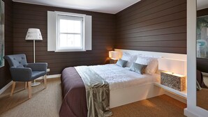 Una camera da letto con un letto, lampade da comodino, una sedia, una finestra e un quadro appeso al muro.