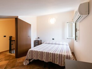 Um quarto pequeno e bem organizado, com cama, mesa de cabeceira, penteadeira, porta e ar condicionado.