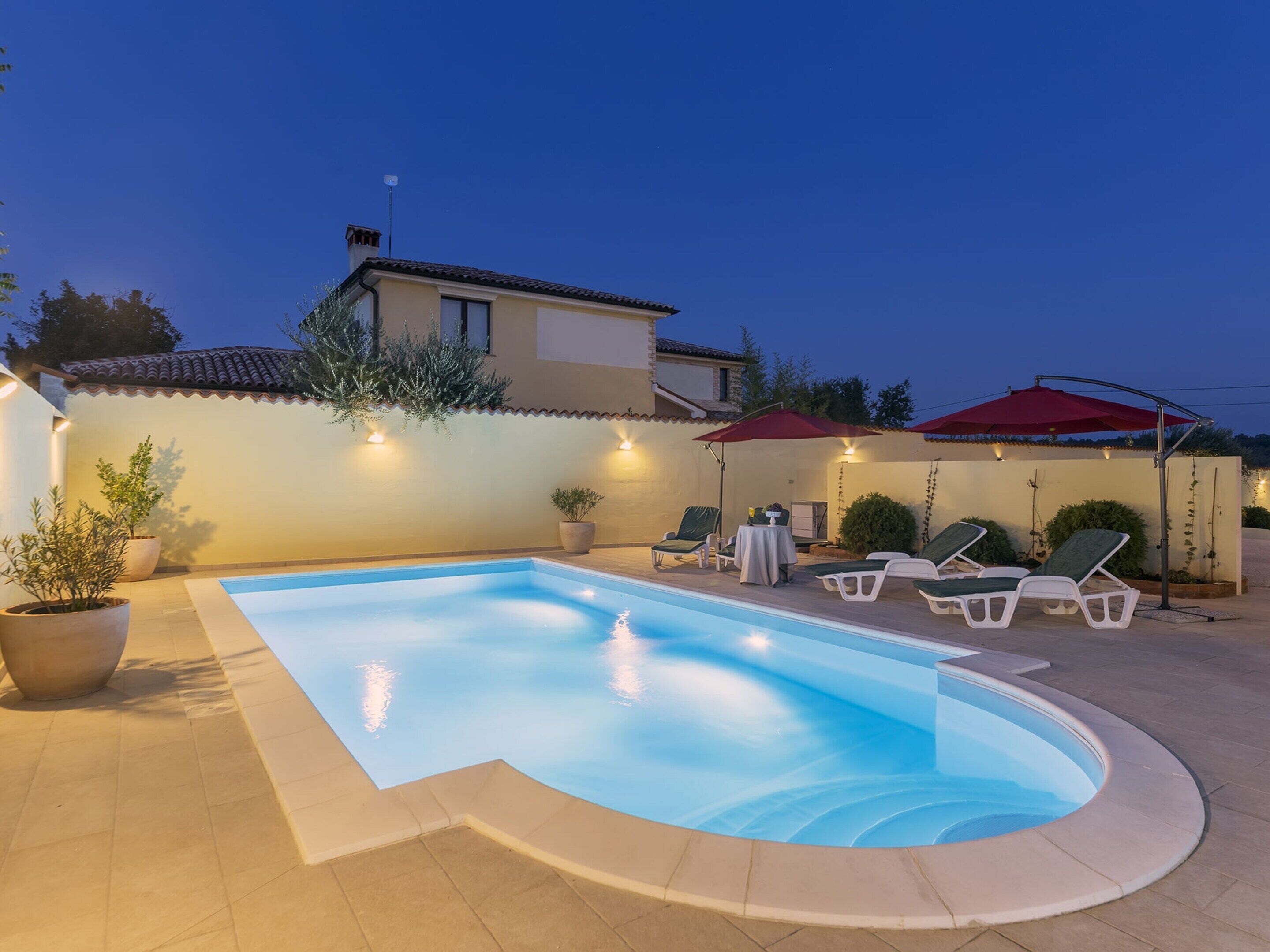 Una piscina con lettini e ombrelloni, circondata da un patio piastrellato e un edificio con tetto in tegole.