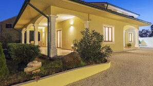 Ένα διώροφο σπίτι με σκεπαστή βεράντα, ένα μονοπάτι από πέτρα και έναν καλά περιποιημένο κήπο.