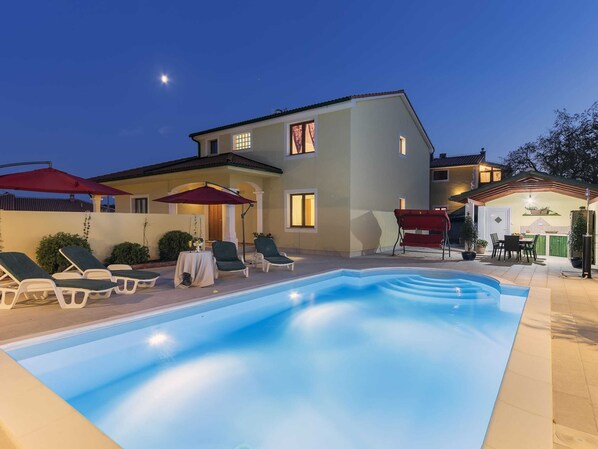 Relax by the rectangular pool surrounded by a deck, lounge chairs, and a shaded table.
