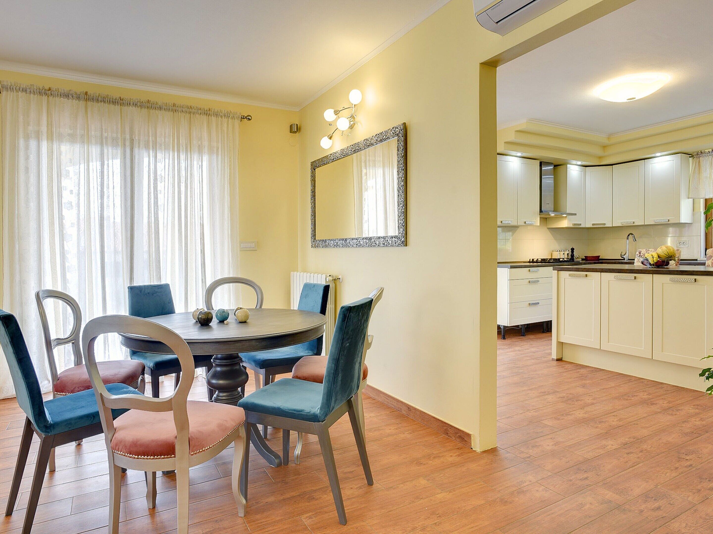 A dining area with a round table and chairs, a kitchen with white cabinets, and a mirror on the wall.