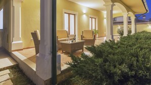 Ένας εξωτερικός χώρος με αίθριο, με σκεπαστή περιοχή για καθιστικό, γλάστρες με φυτά και μια είσοδο με καλό φωτισμό.