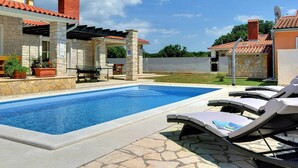 Une piscine avec des chaises longues, des murs en pierre et un patio couvert.