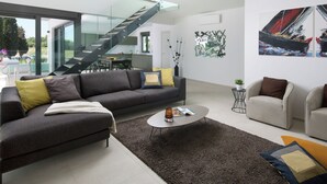 Una sala de estar moderna con un sofá gris, una mesa de centro redonda y una escalera que lleva a un nivel superior.
