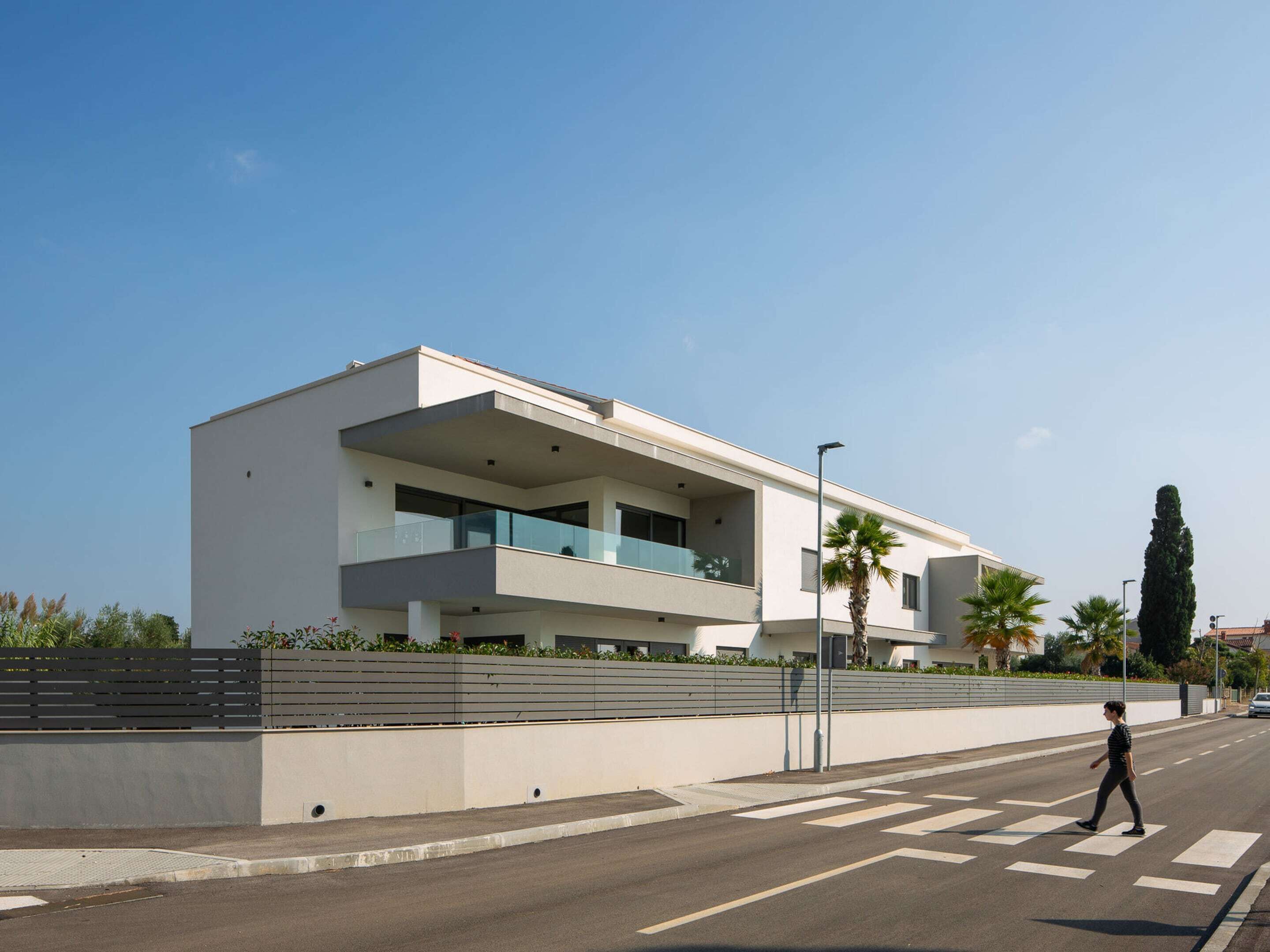 Un bâtiment moderne à deux étages, doté de balcons, d’un passage piéton et surplombant un ciel dégagé.