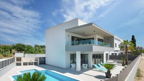 Una casa moderna de dos pisos con piscina, mobiliario exterior y un balcón.