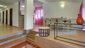 Un intérieur moderne avec un escalier menant à un espace repas, comprenant une table et des chaises, un vase et une vue sur un rideau rose.