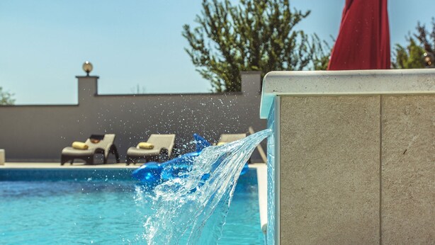Une piscine avec de l’eau qui éclabousse, des chaises longues et un parasol rouge en arrière-plan.