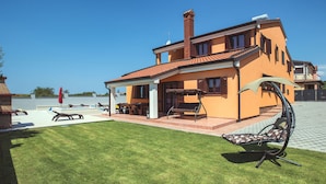 Une maison à deux étages avec une piscine, un espace extérieur aménagé et une vue dégagée sur l’eau.