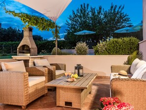 Un espace extérieur aménagé en terrasse, avec des meubles en osier, un four à pizza en pierre et des parasols.