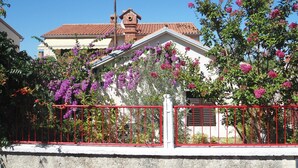 A house with a red roof, surrounded by a red fence, and blooming pink flowers. - Lovely Apartment Near the Sea & the Center (Medulin)