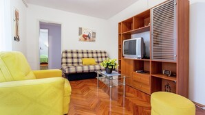 A living room with a sofa, two yellow armchairs, a glass coffee table, and a wooden TV stand with a television. - Lovely Apartment Near the Sea & the Center (Medulin)