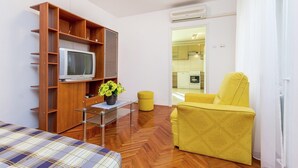 A compact living space with a wooden TV stand, a yellow armchair, a plaid sofa, and a small table with a potted plant. - Lovely Apartment Near the Sea & the Center (Medulin)