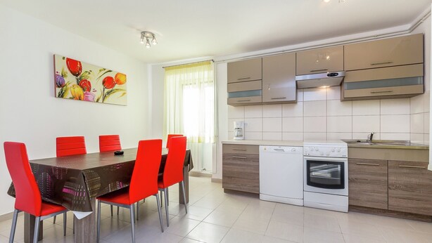 A modern kitchen with a dining area, featuring a table with red chairs, a coffee maker, and a dishwasher. - Lovely Apartment Near the Sea & the Center (Medulin)
