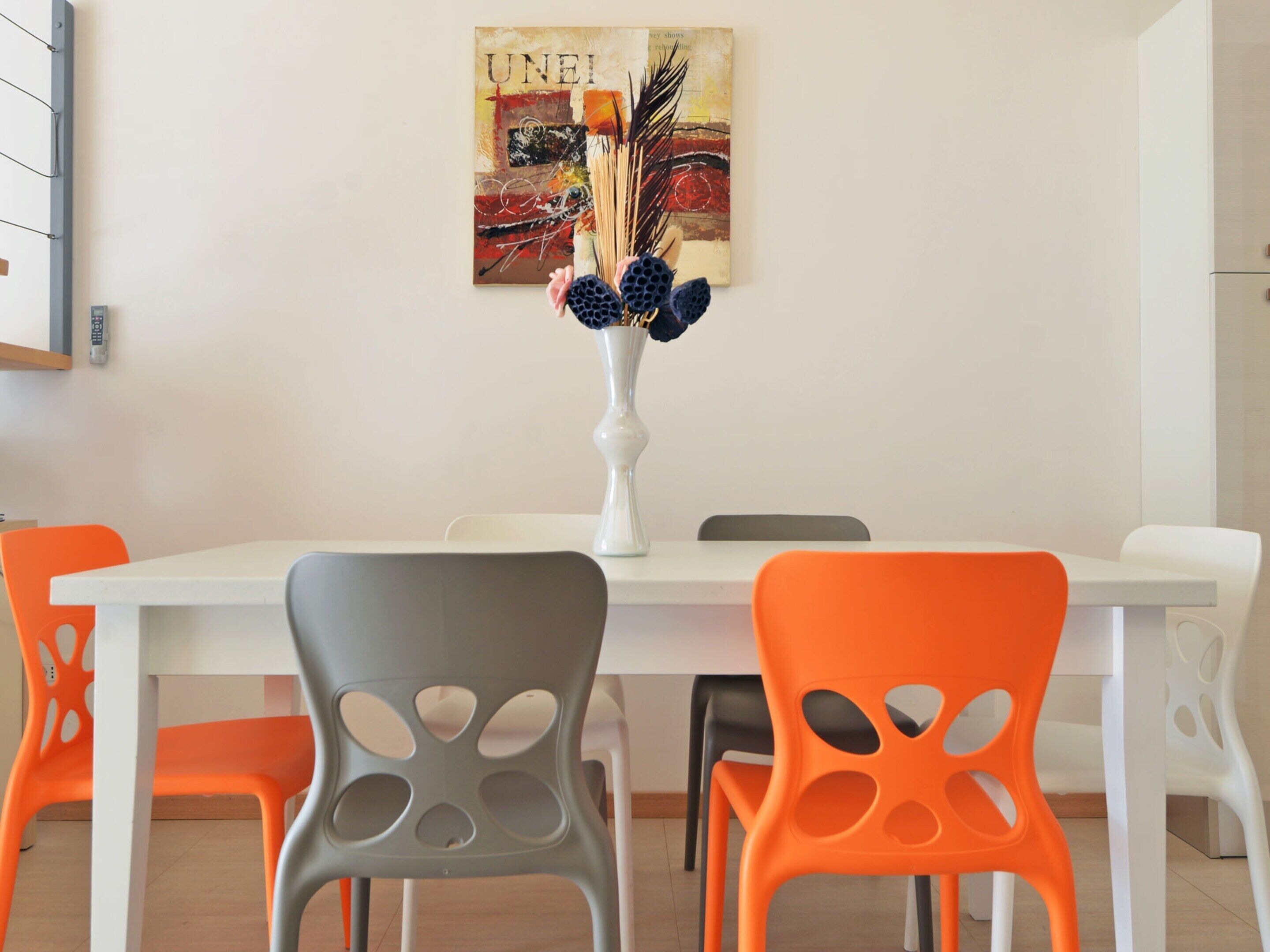 A dining area with a white table and chairs, a vase with flowers, and a painting on the wall.