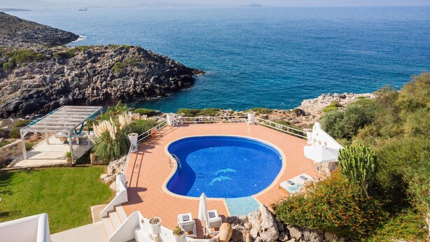 A pool with a curved edge, surrounded by a patio area with lounge chairs and a small table. - Luxury Villa With Amazing Sea Views, Private Pool, Near the Beach (Chania)