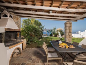 An outdoor patio with a stone fireplace, wicker furniture, and a table set with food and drinks. - Luxury Villa With Amazing Sea Views, Private Pool, Near the Beach (Chania)