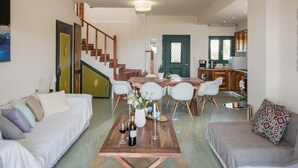 A spacious living area with a wooden coffee table, white sofas, a dining table with chairs, and a staircase leading to another level. - Luxury Villa With Amazing Sea Views, Private Pool, Near the Beach (Chania)