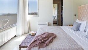 Un dormitorio con una cama grande, una mesita de noche con libros, una ventana con cortinas y vistas al exterior.