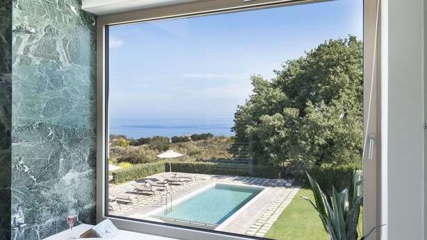 Un baño con un ventanal grande con vistas a una piscina y jardín.