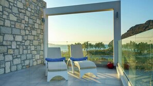 A balcony with two white lounge chairs, a stone wall, and a glass barrier overlooking a coastal landscape. - Villa in Plakias Near the Beach (Agios Vasileios)