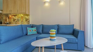 A modern living room with a blue sofa, a small white table, and a stack of colorful plates. - Villa in Plakias Near the Beach (Agios Vasileios)