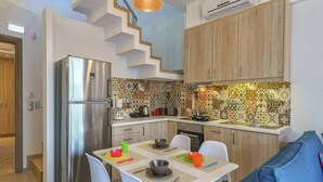 A modern kitchen with a stainless steel refrigerator, a dining table with chairs, and a staircase leading to another level. - Villa in Plakias Near the Beach (Agios Vasileios)
