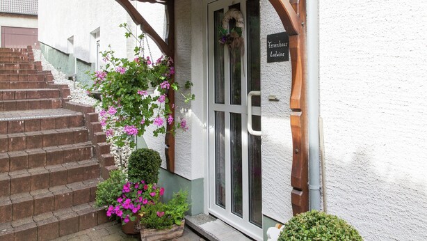 A building entrance with a wooden staircase, a hanging flower basket, and a sign reading "Ferienhaus Ludwine". - Attractive Apartment in Bettenfeld With Garden (Bettenfeld)
