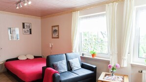 A room with a bed, a sofa, a small table with a vase, and a window with curtains. - Attractive Apartment in Bettenfeld With Garden (Bettenfeld)